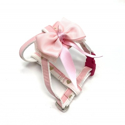 Peitoral para cão branco e rosa com padrão de corações e laço rosa.