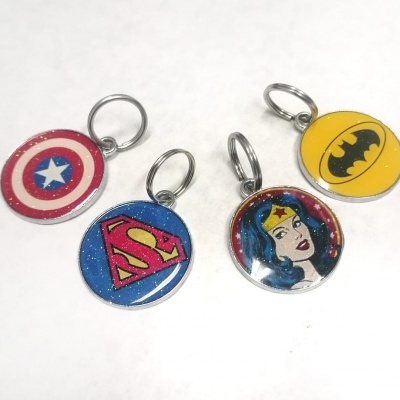 Quatro porta-chaves redondos com símbolos dos super-heróis Capitão América, Super-Homem, Mulher Maravilha e Batman