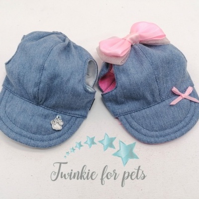 Dois bonés pequenos para cães azuis em tecido jeans com laços cor de rosa e texto da marca em fundo branco