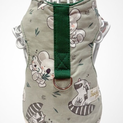 Colete para cão tecido bege com estampado de animais e fita verde com anilha metálica.