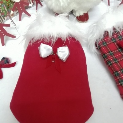 Capa vermelha para cão com laço branco e pelúcia na gola em cenário natalício