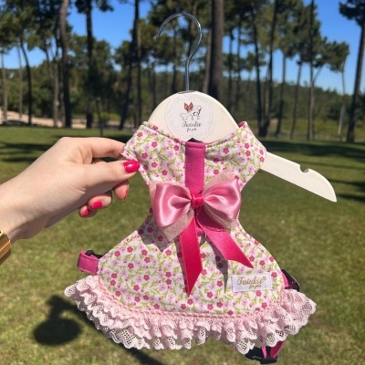 Vestido para cão rosa com padrão floral e laço em cabide branco ao ar livre