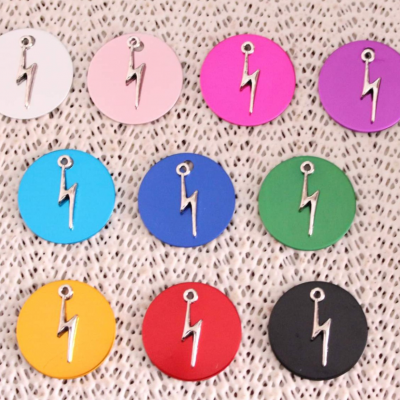 Dez medalhões coloridos circulares com um pingente de raio prateado sobre tecido bege entrelaçado