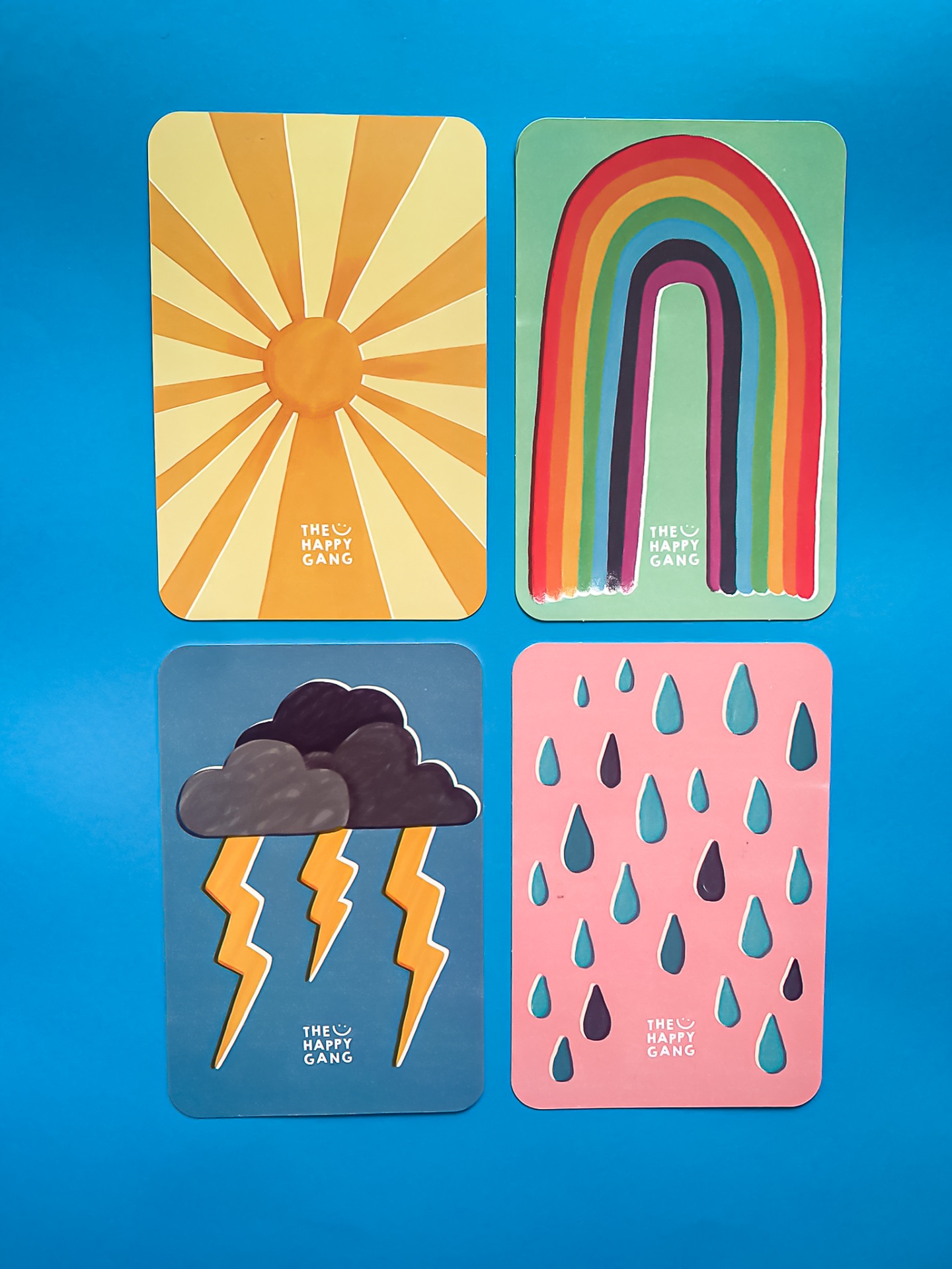 Quatro cartões coloridos com sol, arco-íris, nuvens com relâmpagos e gotas de chuva