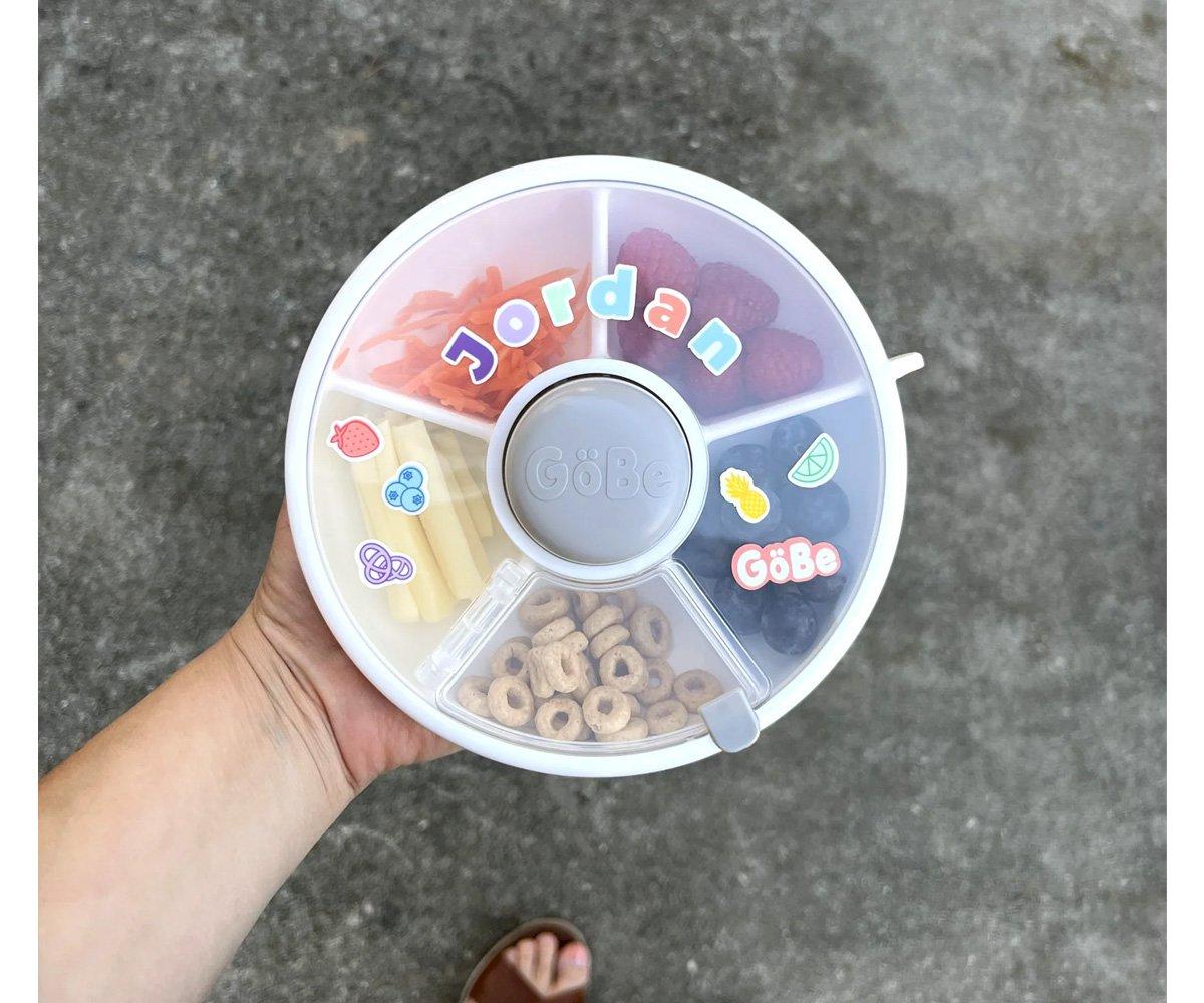 Caixa organizadora redonda de plástico com snacks e etiquetas coloridas