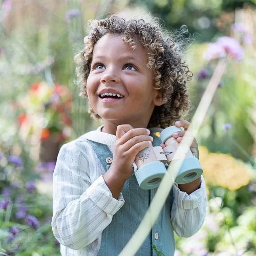 Criança com binóculos azuis coloridos em jardim florido