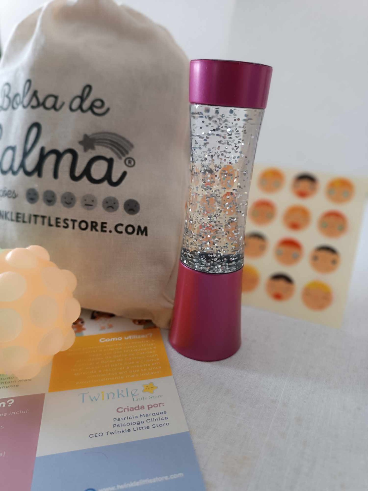 Frasco com glitter e tampa rosa ao lado de bolsa de tecido e folhetos coloridos