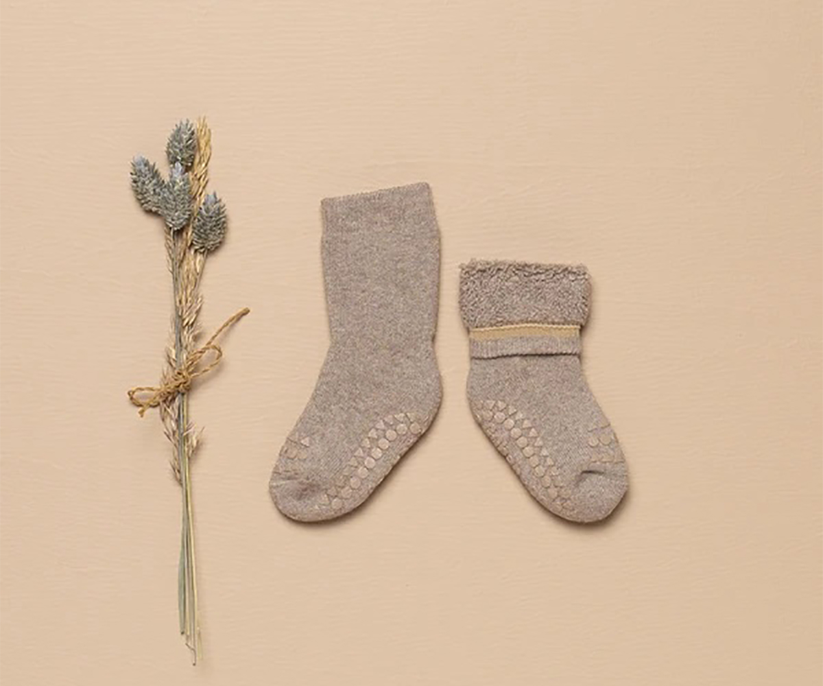 Par de meias cinzentas para bebé com padrão antiderrapante ao lado de ramo seco sobre fundo bege