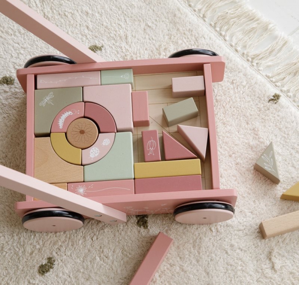 Carrinho de madeira rosa com blocos de construção coloridos em tapete claro