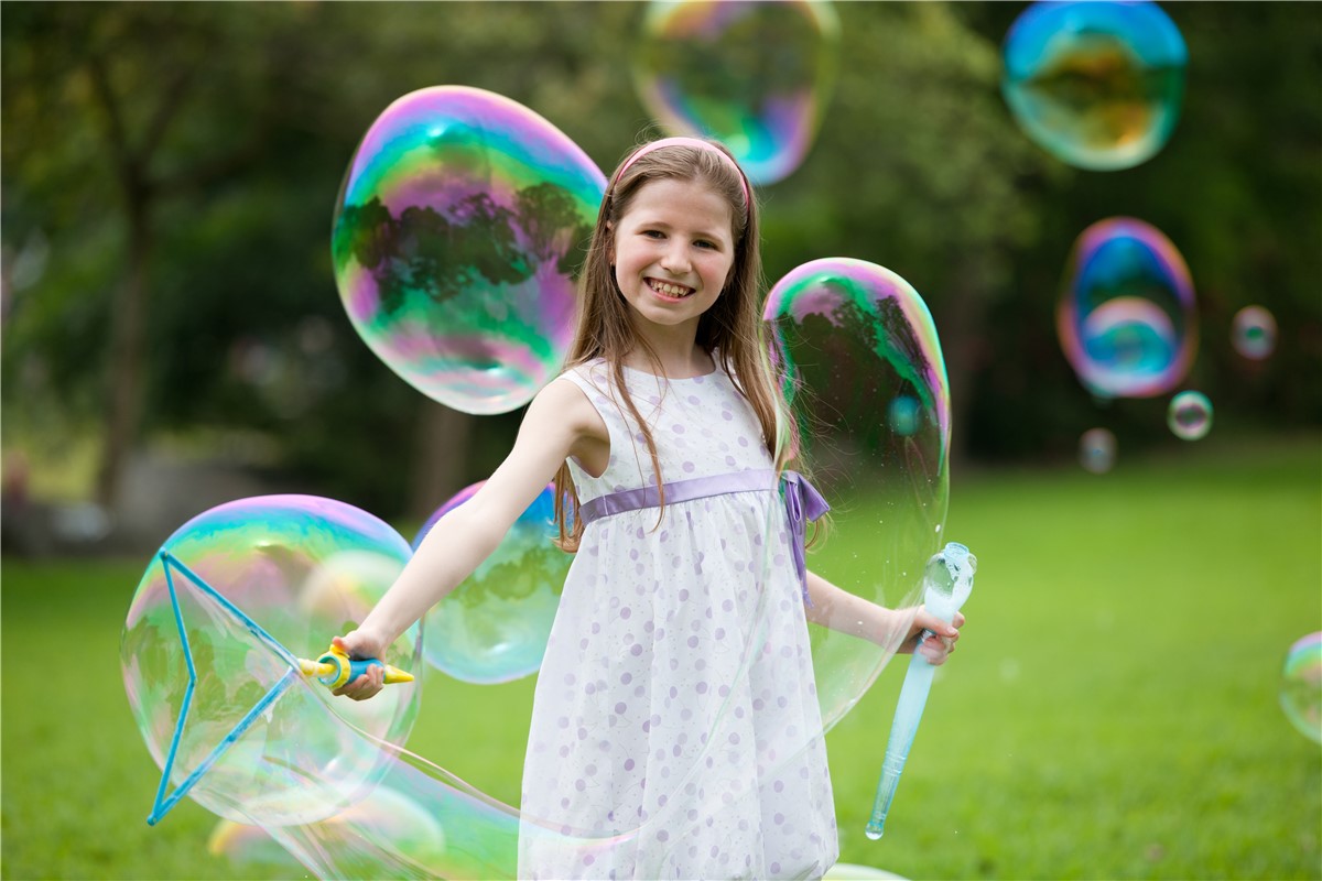 Criança com vestido branco a fazer bolhas de sabão num parque verde
