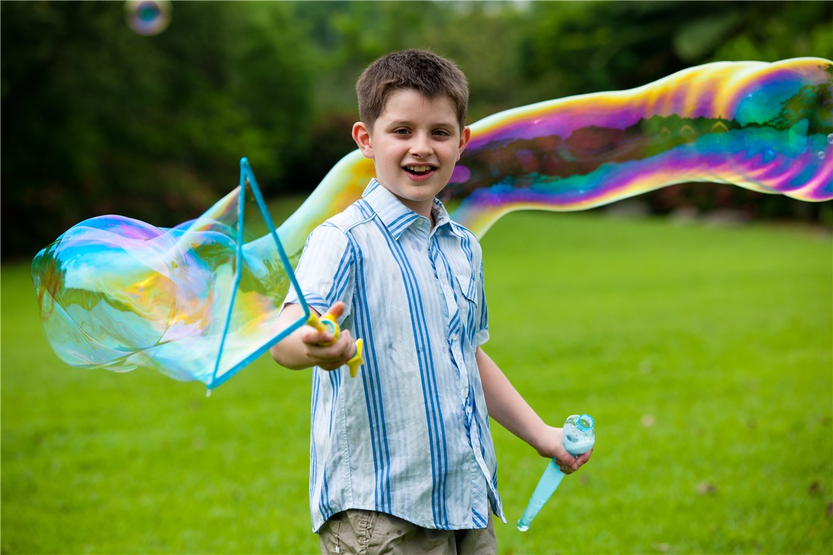 Criança faz bolhas de sabão grandes ao ar livre com dispositivo azul