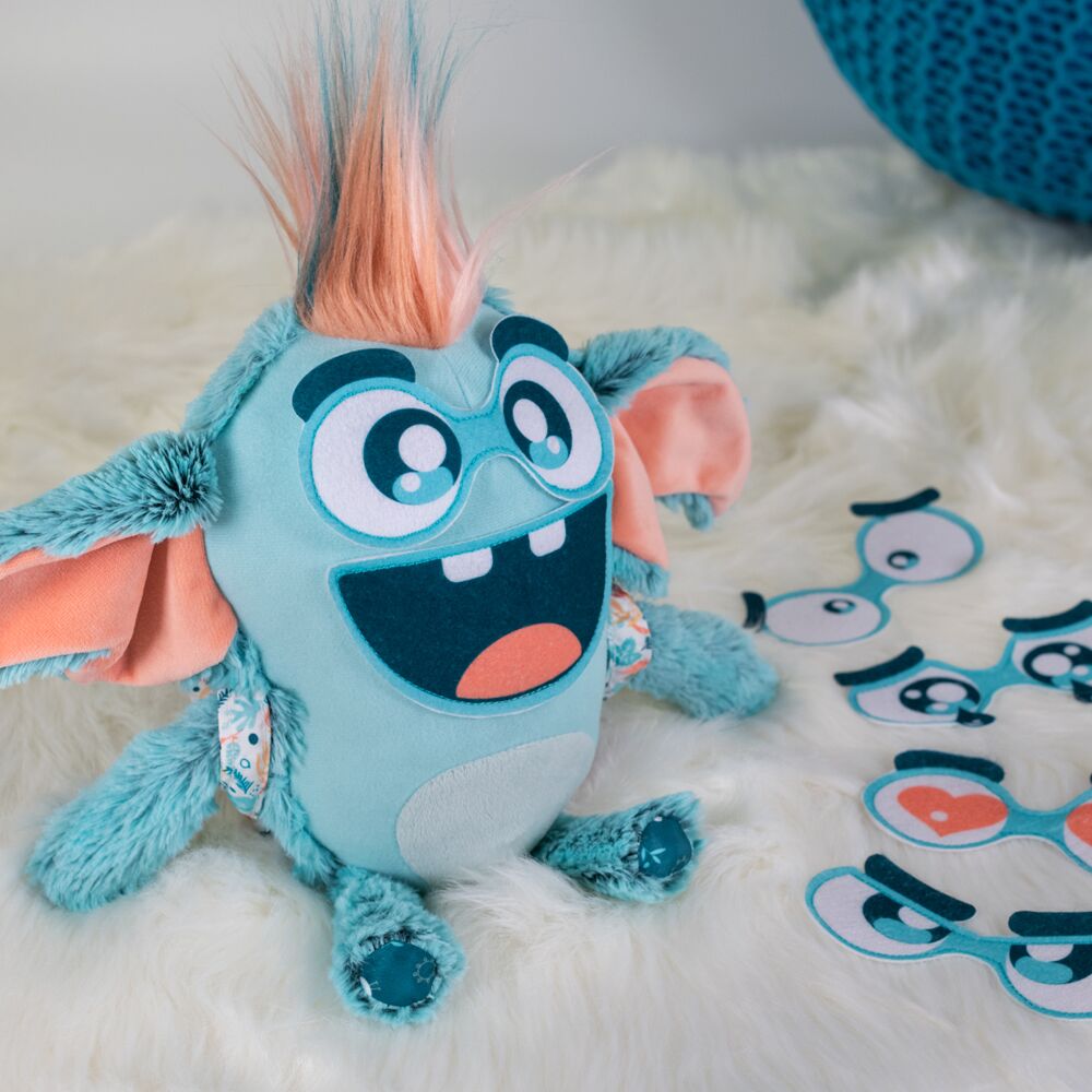 Pelúcia azul com rosto grande e pêlo colorido, com peças faciais destacáveis ao lado