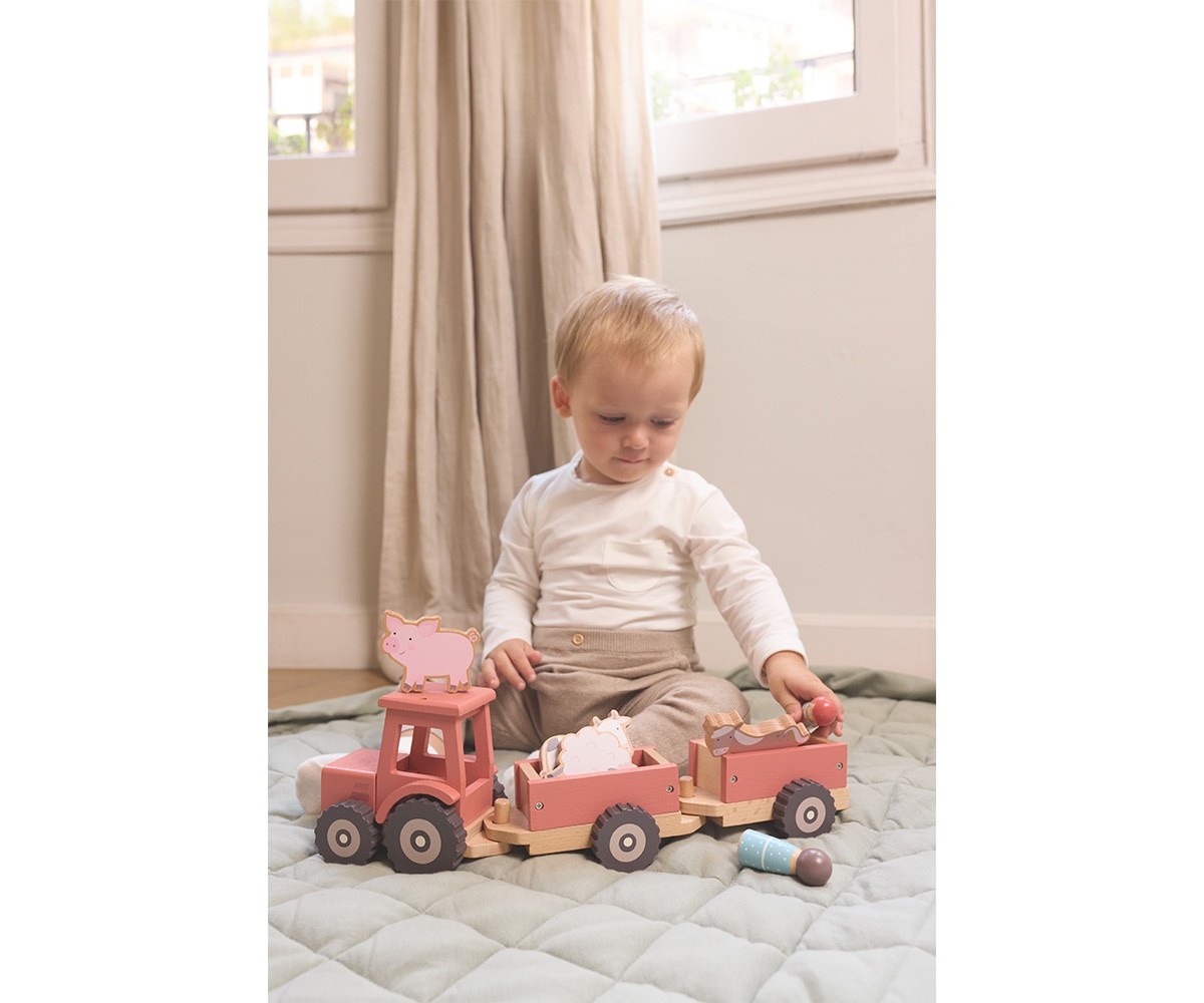 Criança com brinquedo de madeira em forma de trator rosa com reboques contendo figuras de animais