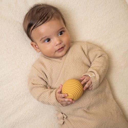 Bebé com conjunto de malha bege segurando bola amarela