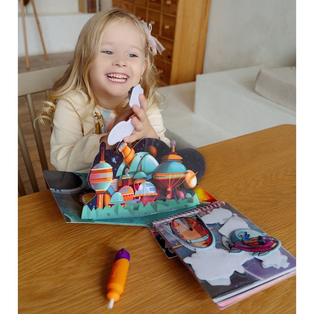 Menina loira a brincar com livro pop-up colorido numa mesa de madeira