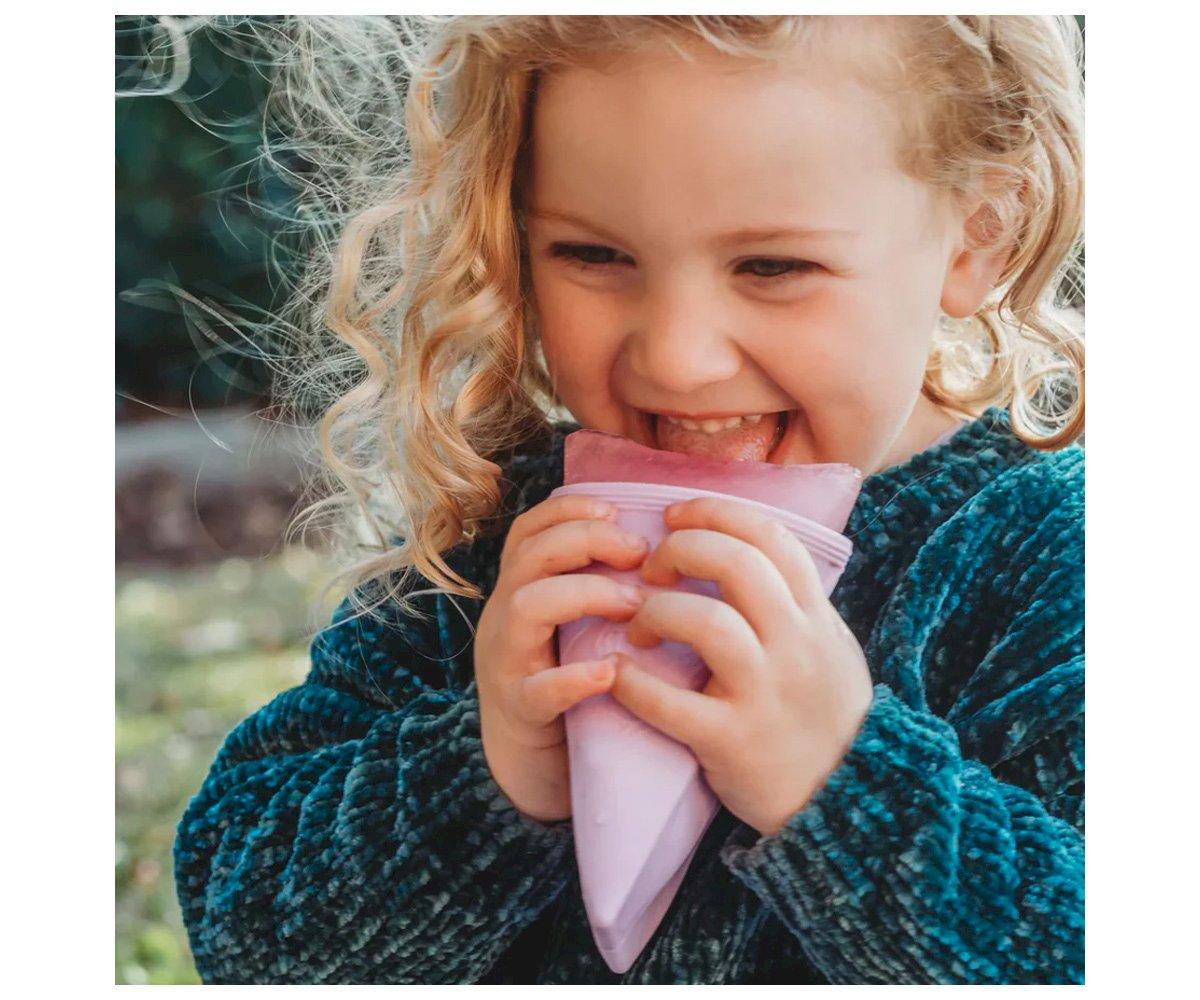 Criança loira segurando saco de alimento rosa ao ar livre