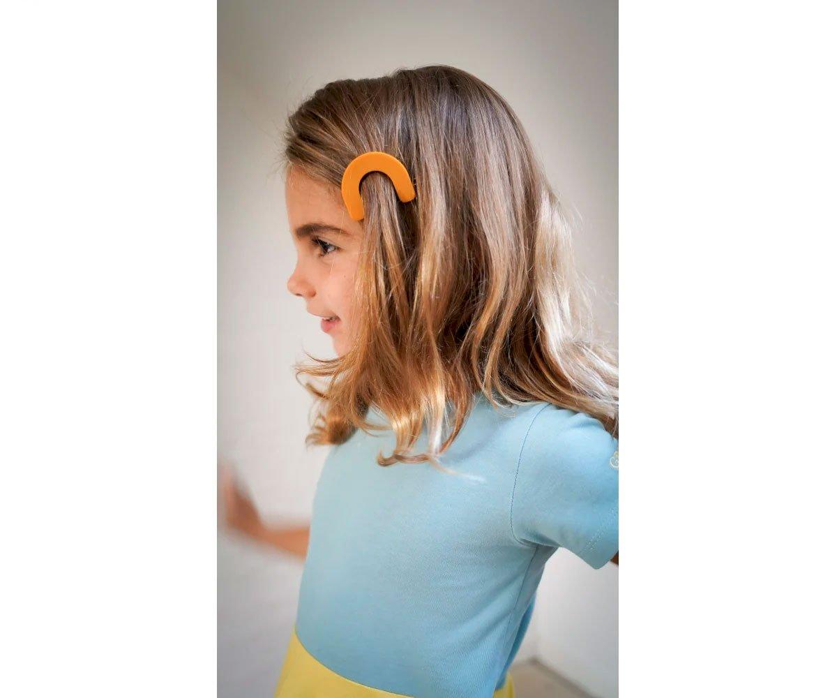 Criança loira com presilha de cabelo laranja