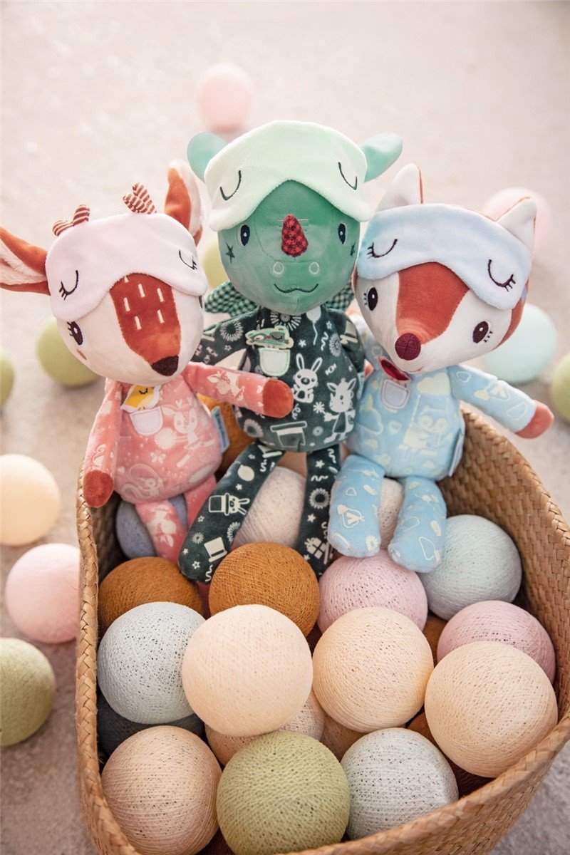 Três bonecos de pelúcia sentados numa cesta com bolas decorativas coloridas em tons pastel.