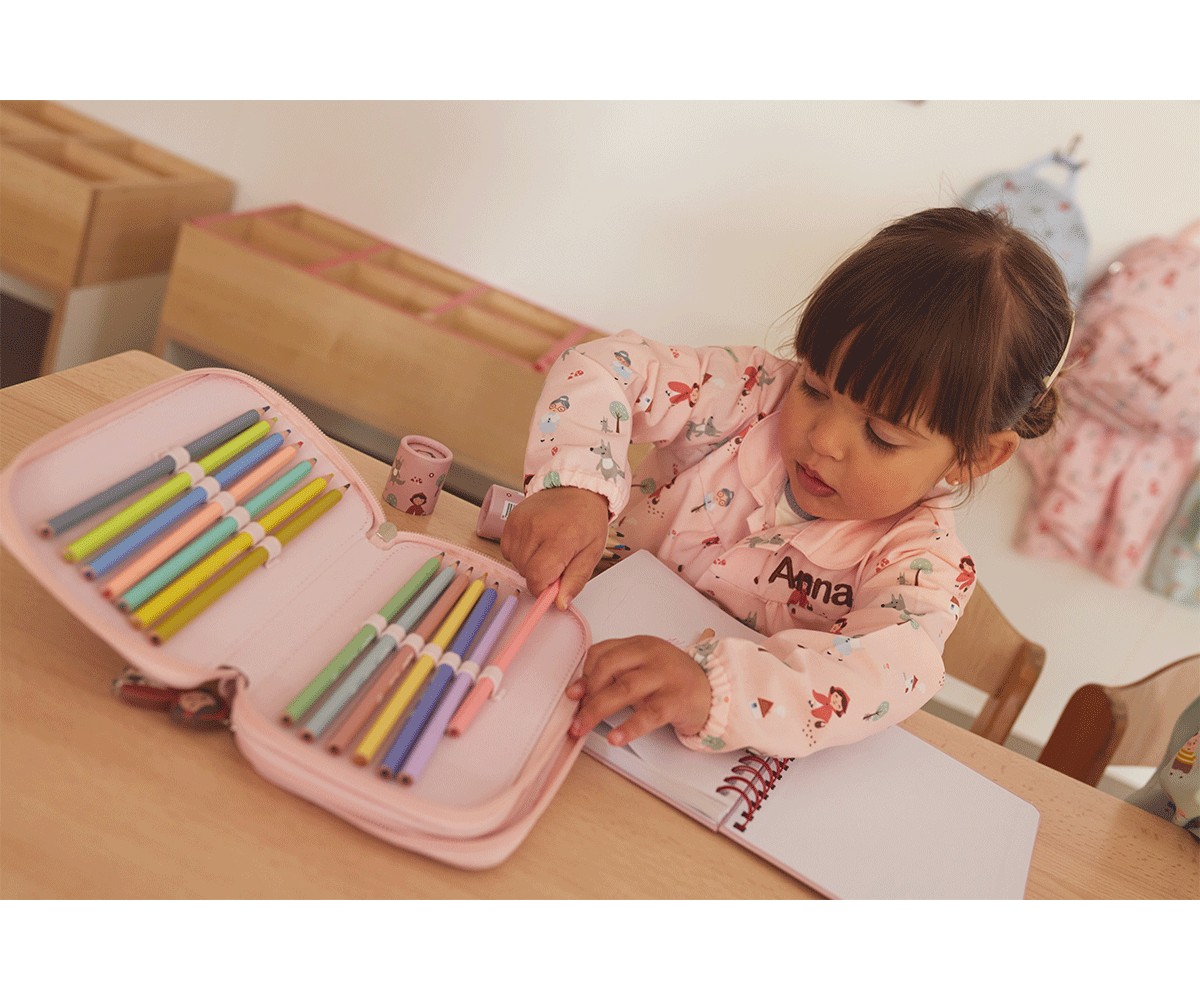 Estojo rosa aberto com lápis de cores e criança a desenhar num caderno