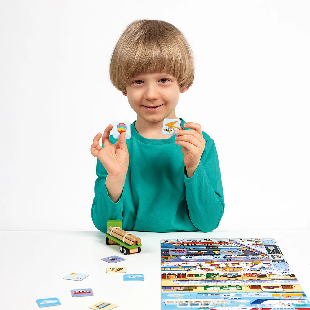 Criança com camisola verde segura duas peças quadradas de jogo em mesa com tabuleiro colorido