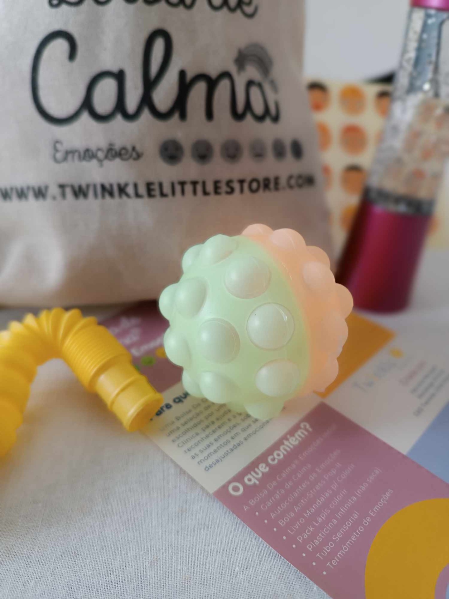 Brinquedo sensorial colorido com esfera texturizada e saco de tecido com texto atrás