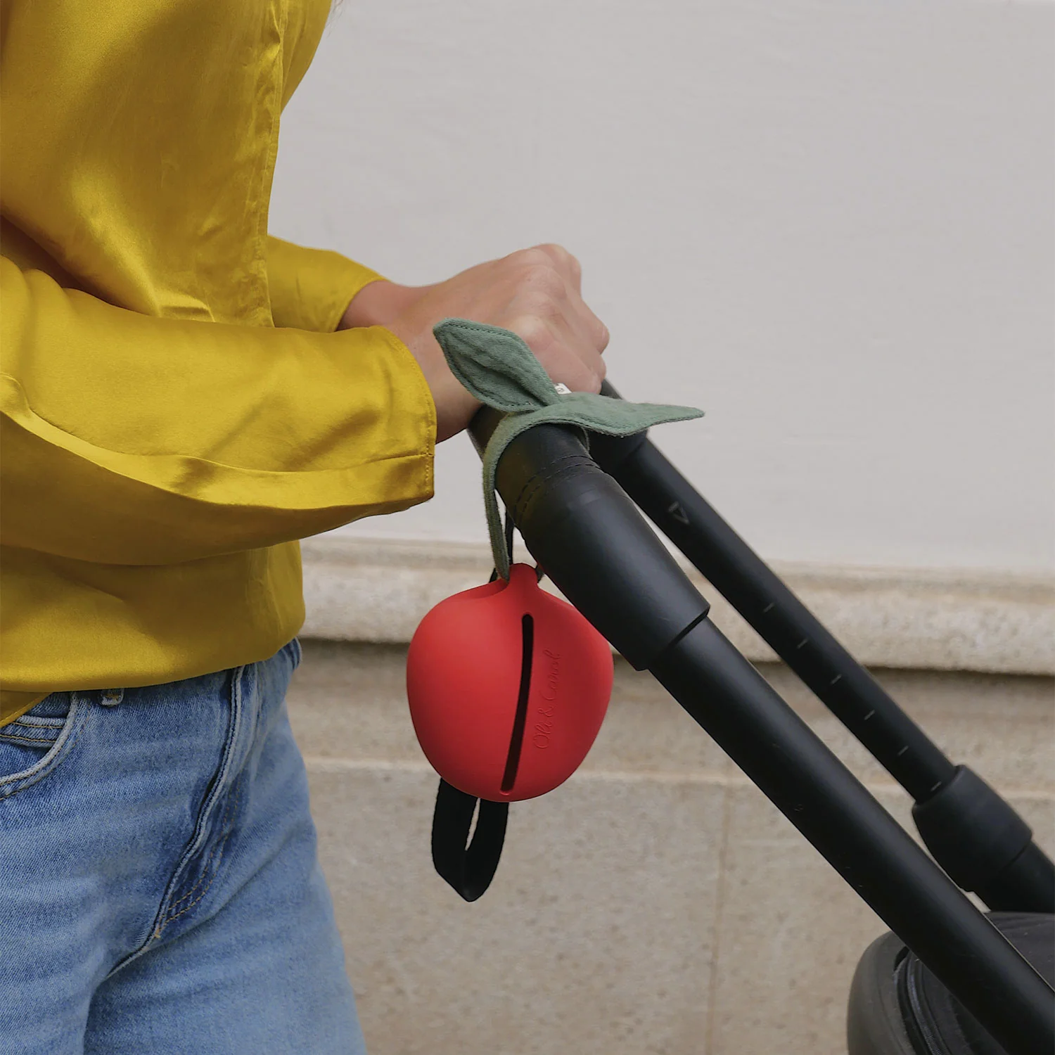 Acessório vermelho em forma de maçã pendurado numa pega de carrinho, com pessoa ao lado em camisa amarela e calças de ganga.
