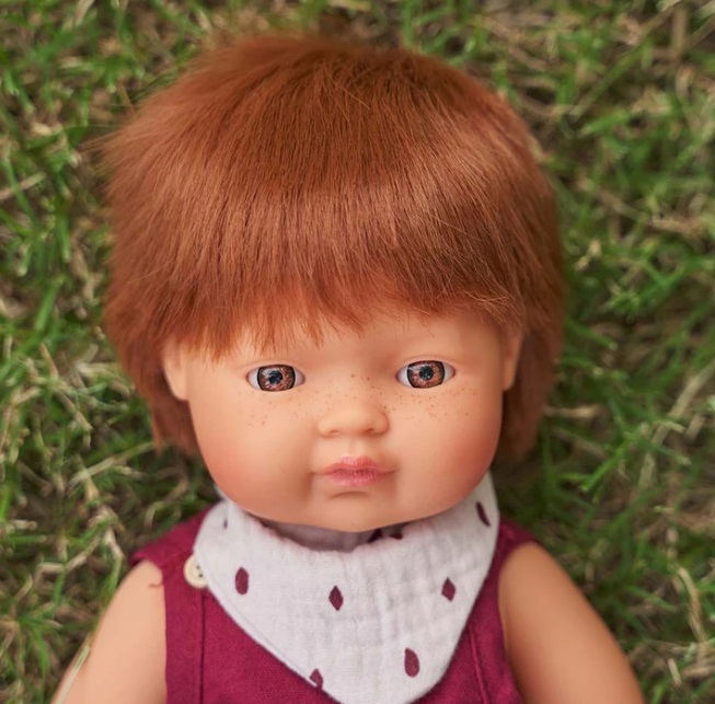 Boneco menino com cabelo ruivo e roupa vermelha sobre relva