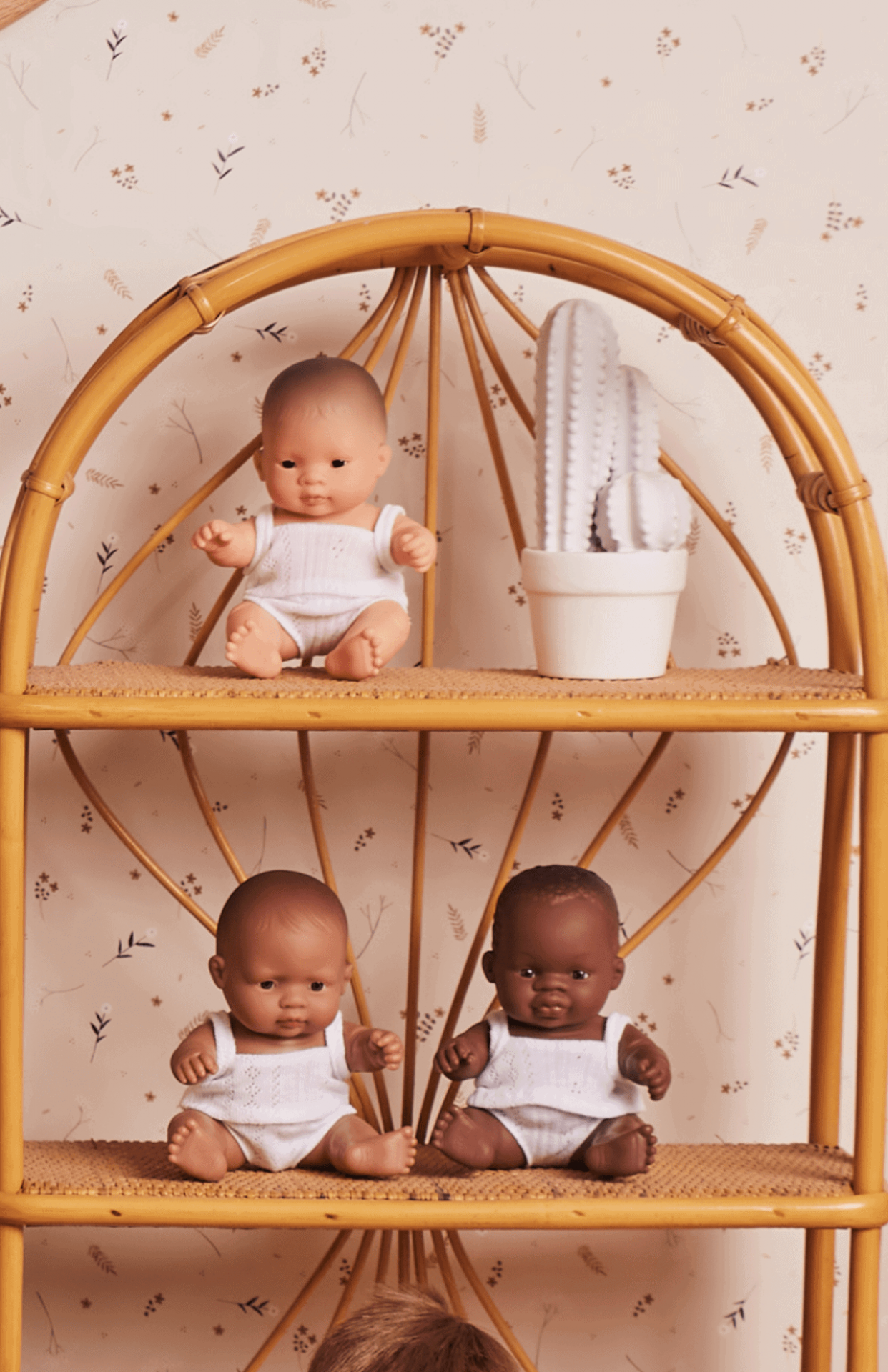 Bonecos bebés em prateleira de rattan com planta decorativa branca