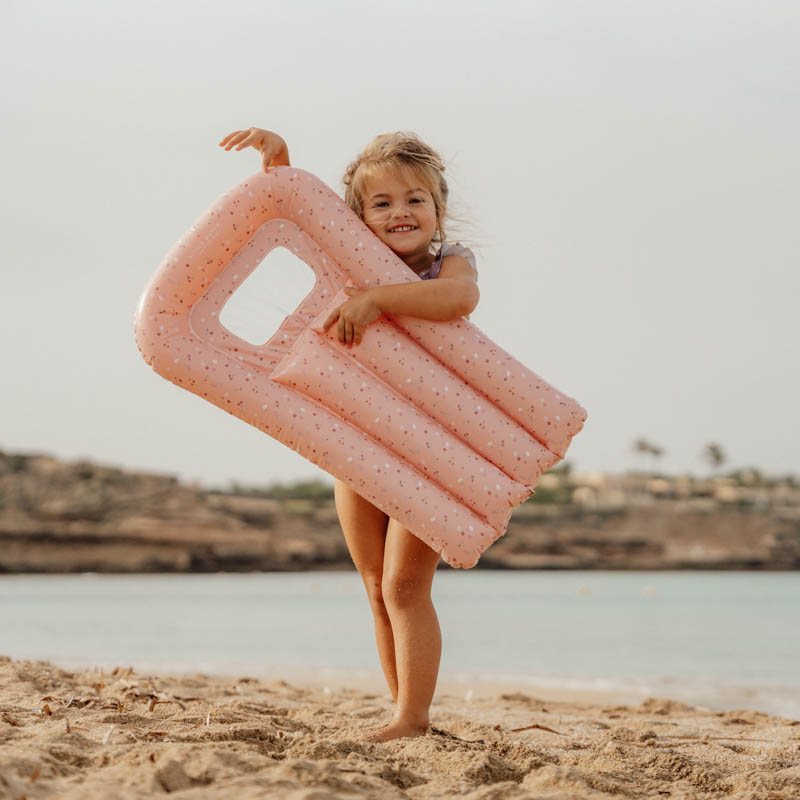 Criança na praia segurando colchão insuflável rosa com pontos pretos