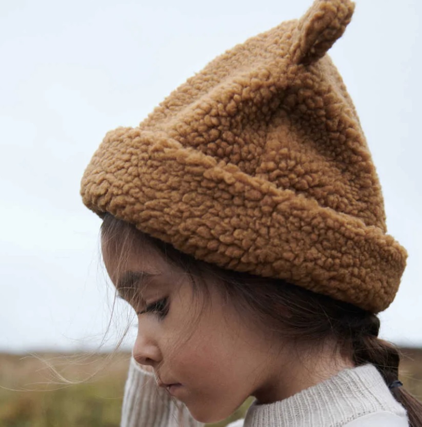 Gorro castanho felpudo com aba dobrada usado por criança de perfil