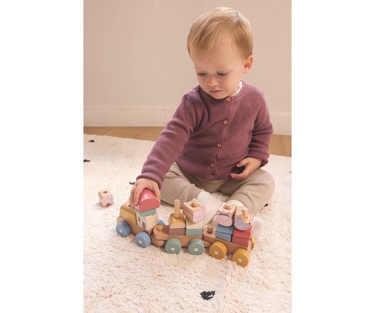 Bebé a brincar com comboio de madeira colorido num tapete creme