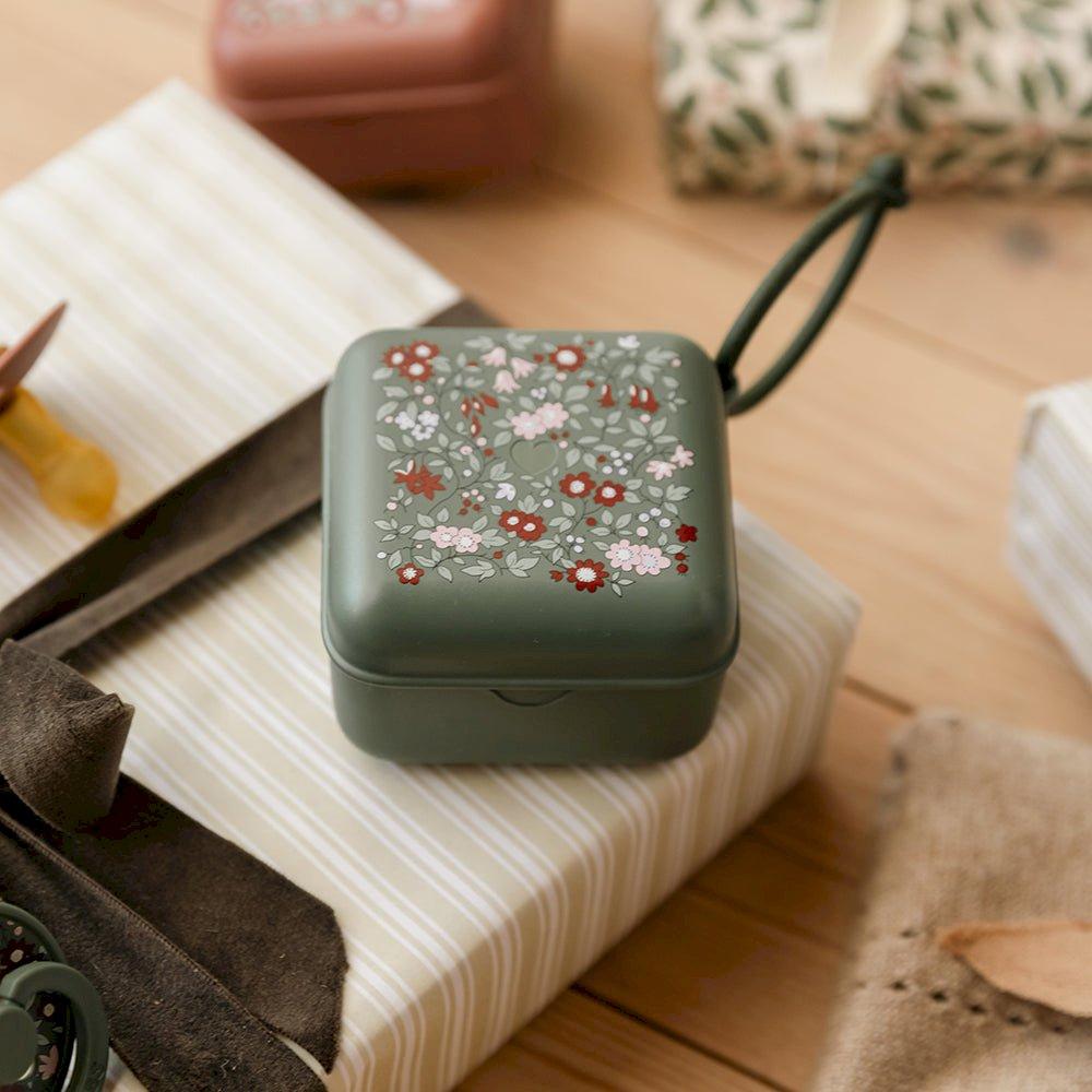 Caixa quadrada verde com padrão floral e alça preta sobre mesa de madeira
