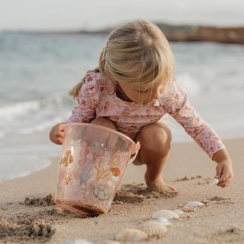 Criança com balde transparente na praia recolhendo conchas na areia