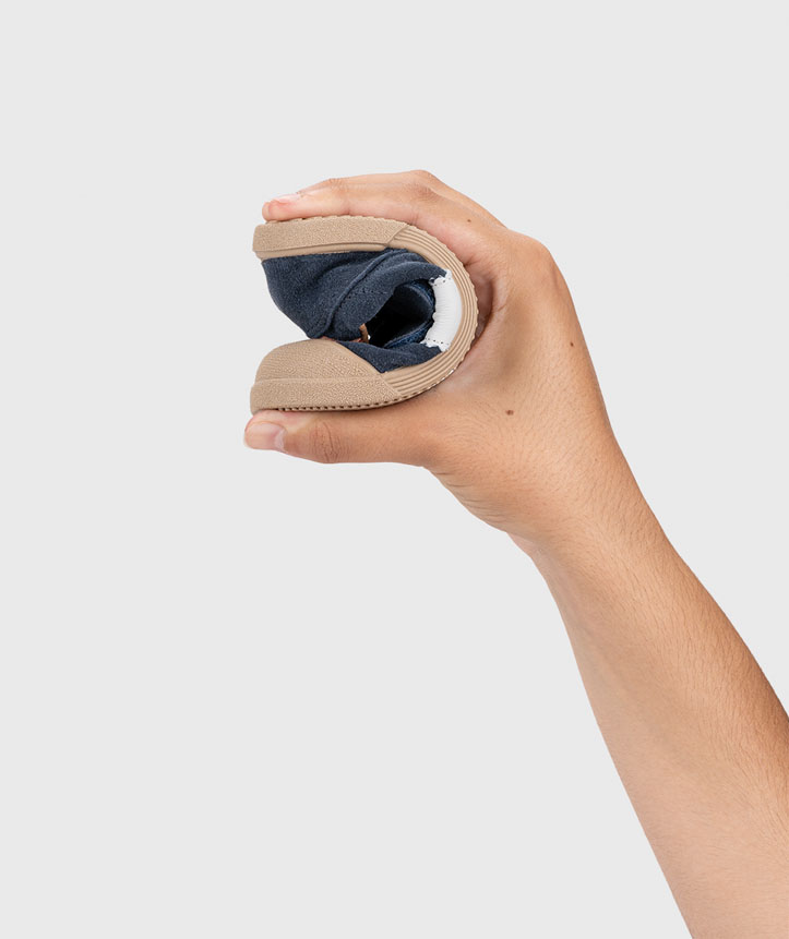 Sapato azul-marinho dobrado ao meio com sola castanha segurado por mão num fundo cinzento