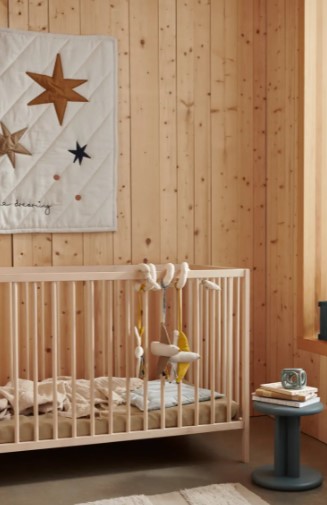 Berço de madeira clara com móbile de tecido pendurado em quarto com paredes de madeira e mesa azul
