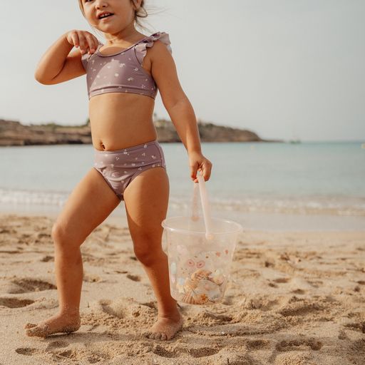 Menina na praia com biquíni lilás de corações e balde transparente com conchas