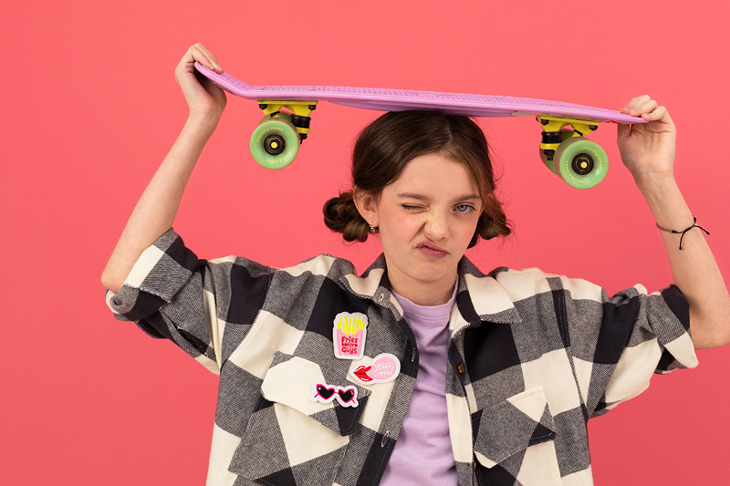 Pessoa jovem com blusa xadrez segura skate cor-de-rosa acima da cabeça