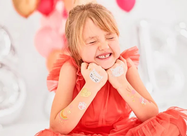 Criança com vestido vermelho e tatuagens temporárias nos braços sorrindo