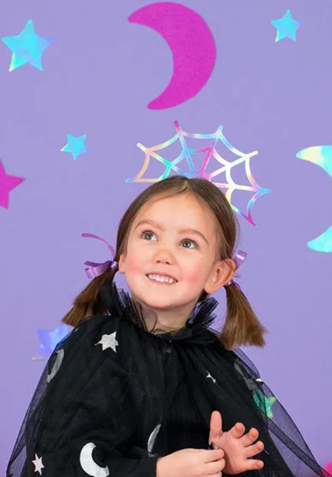 Criança com capa de estrelas e luas e acessório de teia de aranha holográfico na cabeça.