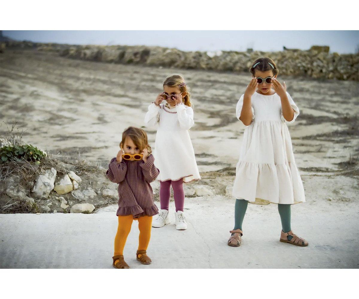 Três crianças com vestidos e collants coloridos num caminho de terra ao ar livre