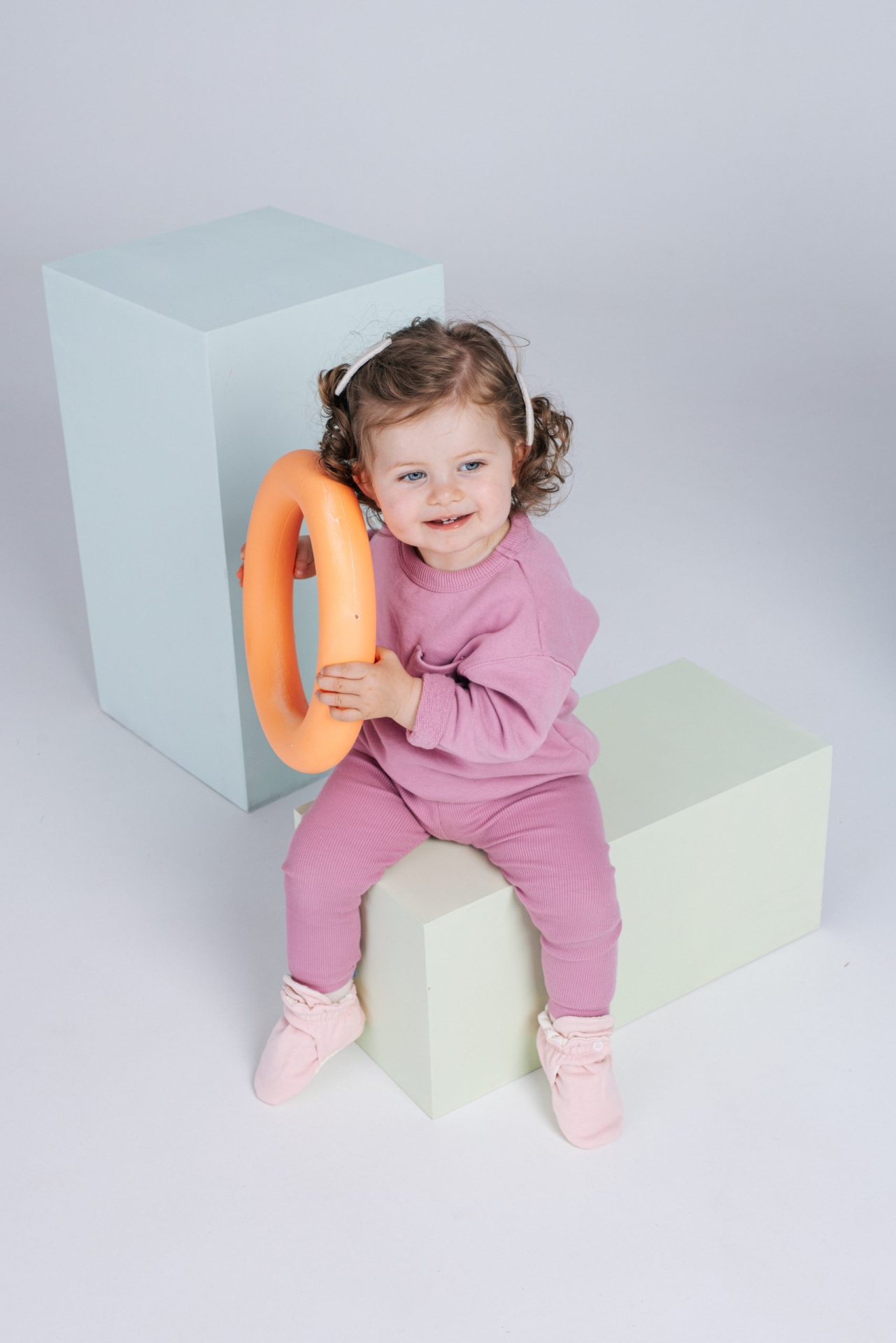 Criança pequena com roupa rosa sentada segurando anel laranja em estúdio branco