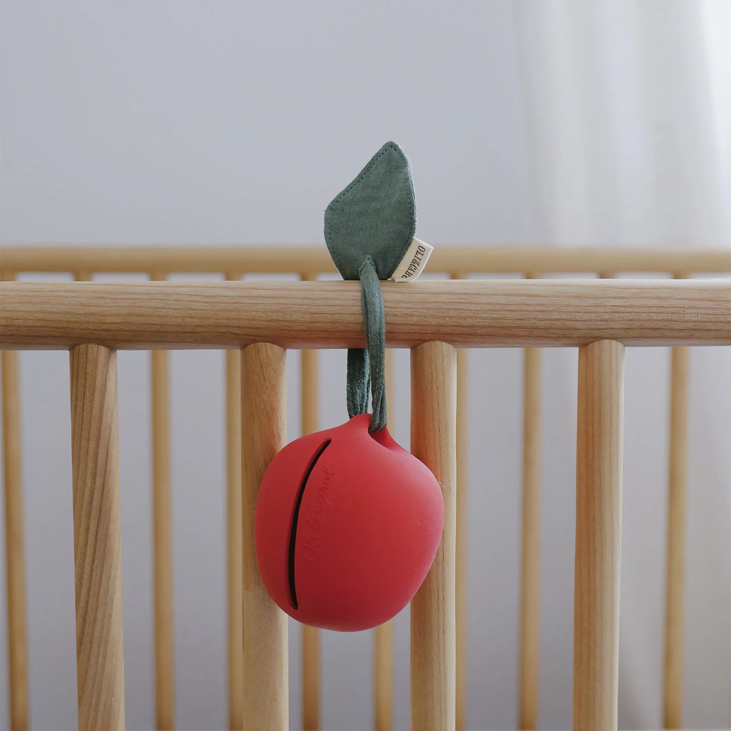 Brinquedo para bebés em forma de maçã vermelha pendurado na cama de grades de madeira clara