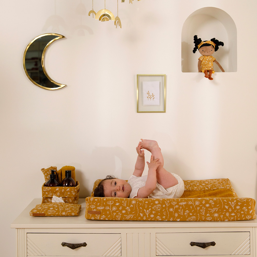 Cama de mudança amarela com bebé deitado e boneca de pano numa alcova na parede branca