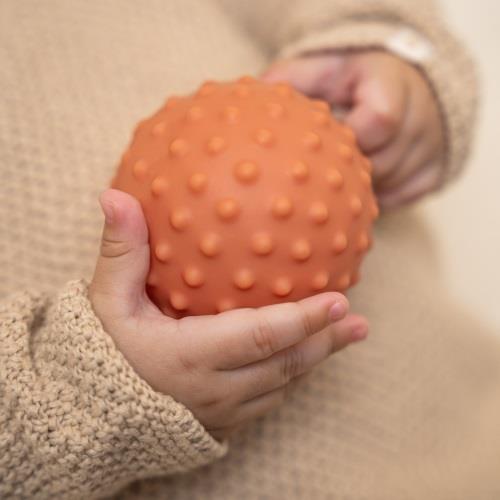 Criança segurando bola laranja com pontos salientes