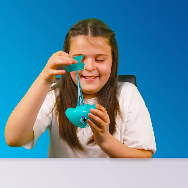 Menina a brincar com plasticina azul elástica sobre superfície branca e fundo azul