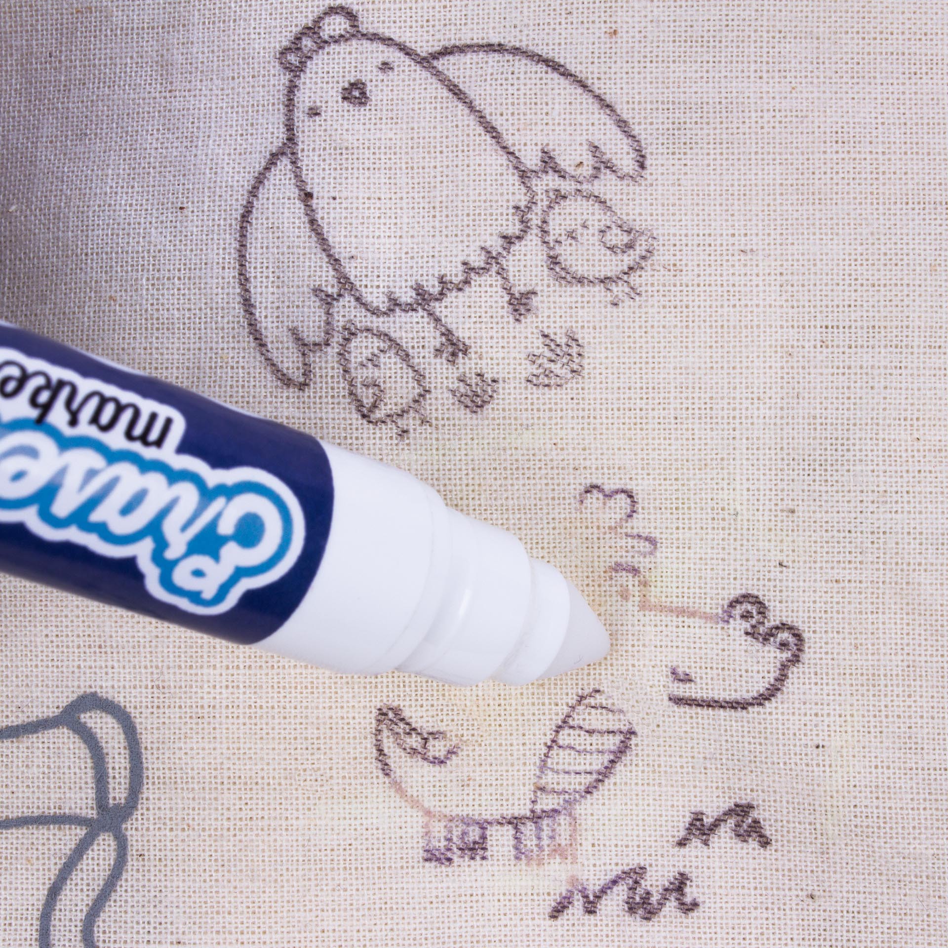 Marcador branco a pintar desenhos a preto numa tela de tecido bege com desenhos de um pássaro e uma tartaruga.