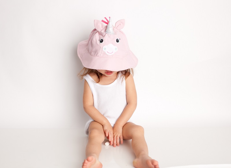 Criança com chapéu rosa de unicórnio e roupa branca sentada