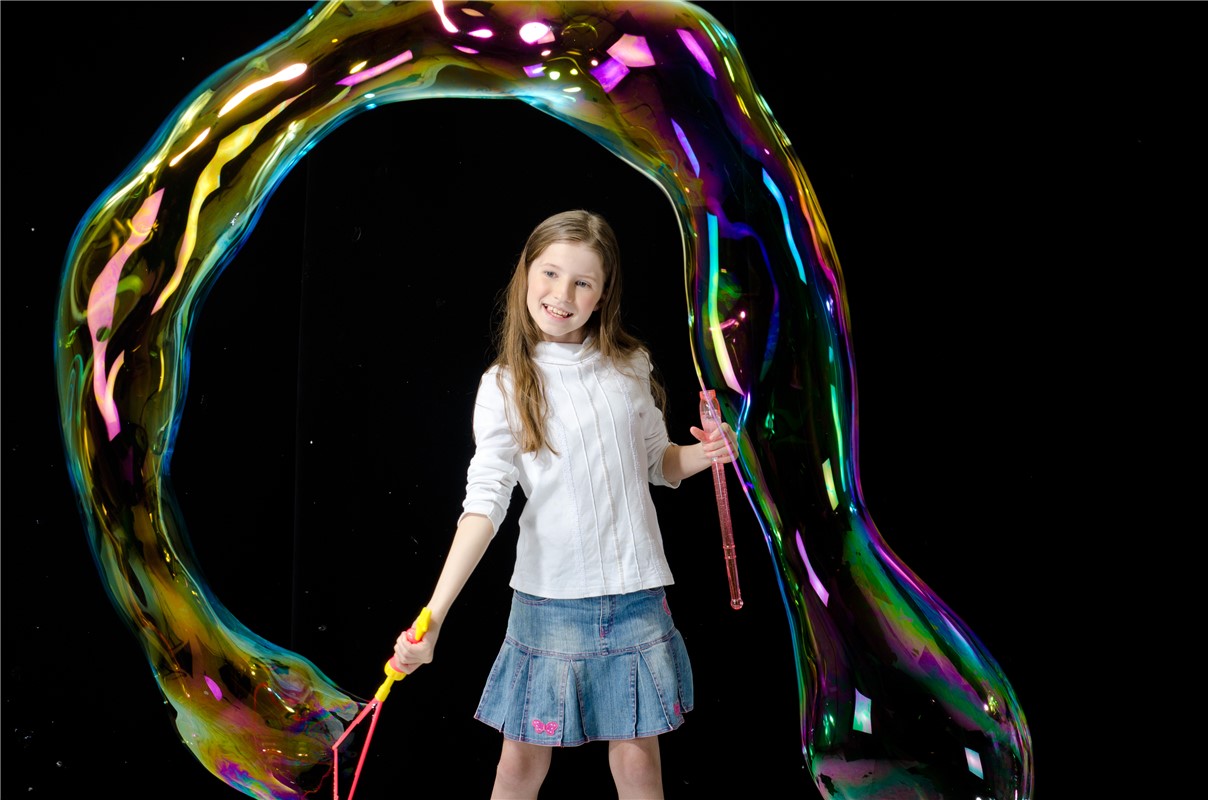 Menina fazendo bolhas de sabão grandes coloridas com varinhas