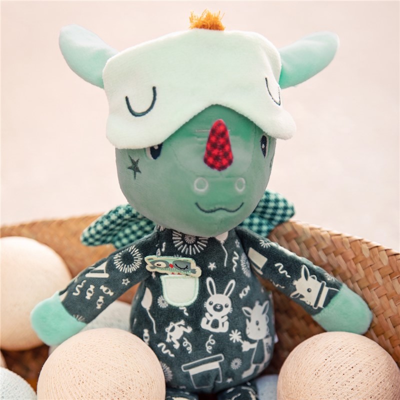 Boneco de peluche verde com pijama estampado e chapéu com orelhas sentado numa cadeira de palha