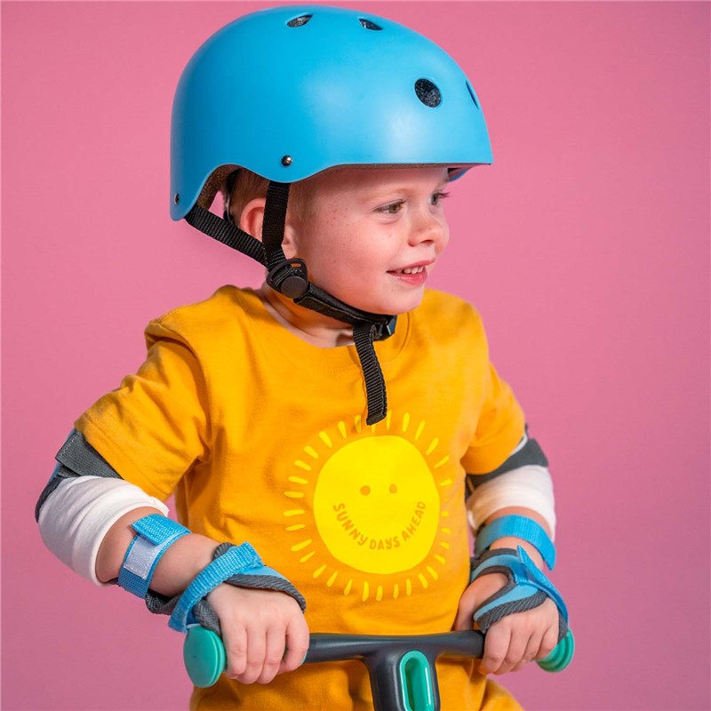 Criança com capacete azul e t-shirt amarela sorrindo segura guidão